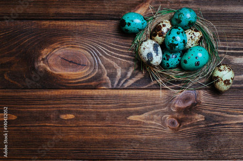 Painted quail eggs in natural nest over rustic wooden background