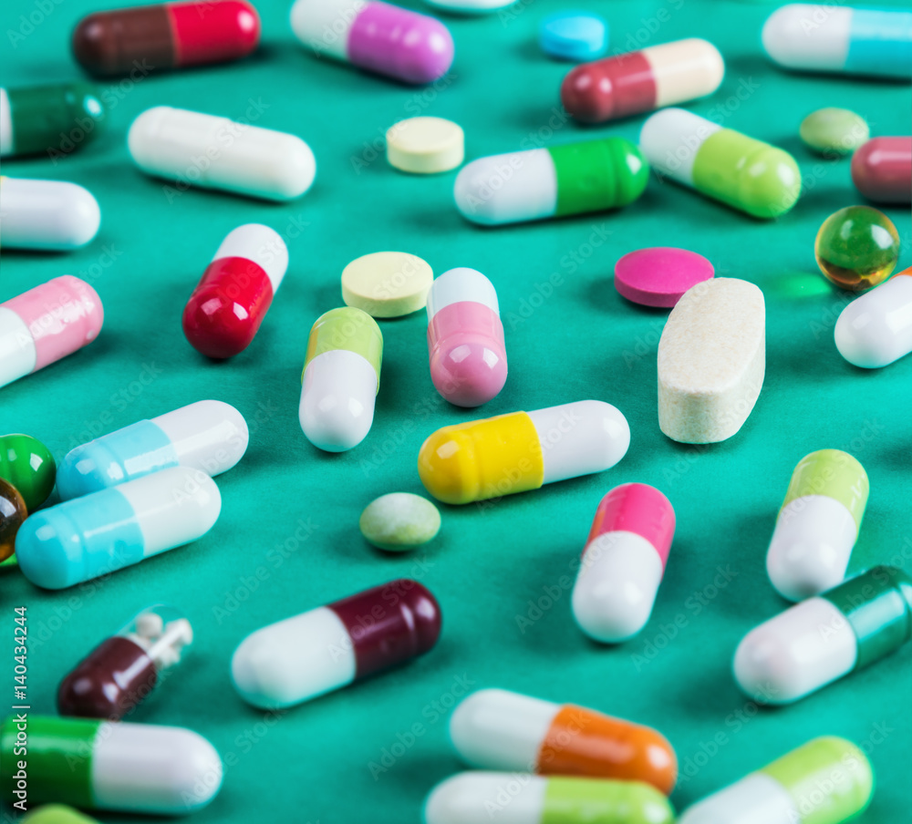 Different colors of pills and a tablet on a green background Different colors of pills and a tablet on a green background