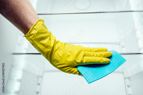 Man's hand cleaning white fridge with blue rag