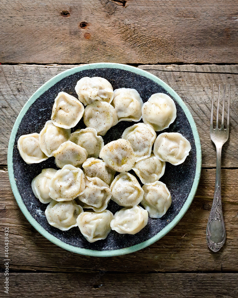 Boiled prepared homemade russian pelmeni, dumplings, ravioli with meat on grey plate with fresh parsley, pepper, wooden rustic background. Top view. Copyspace Boiled prepared homemade russian pelmeni, dumplings, ravioli with meat on grey plate with fresh parsley, pepper, wooden rustic background. Top view. Copyspace