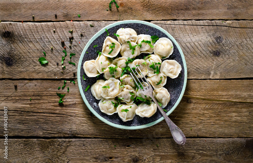 Traditional russian pelmeni, ravioli, dumplings with meat on wooden table with flour, parsley, quail eggs, pepper, rosemary, bay leaf and spices. Top view. Copyspace