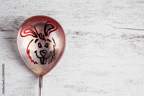 Easter bunny drawing closeup on vintage silver spoon placed on white rustic wooden table with copy space