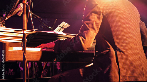 Piano player plays the piano keyboard on the stage with sound lights. Jazz retro vintage concert performance entertainment. Close up shot with selective focus.