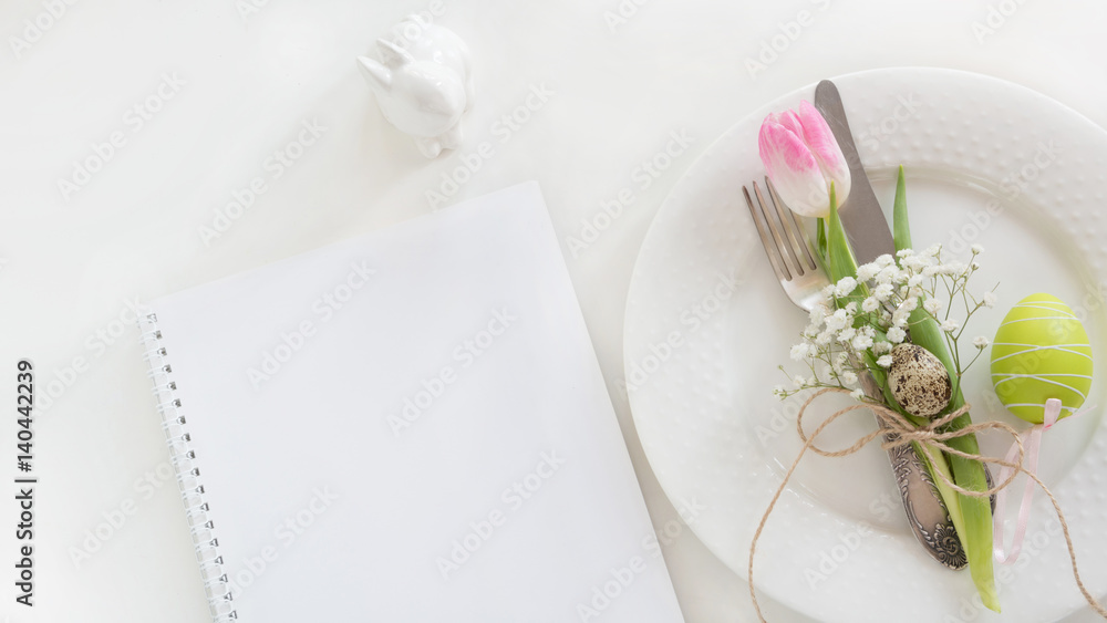 Easter table setting with decor and empty note on white background. Spring romantic dinner. Top view and copy space for your text.