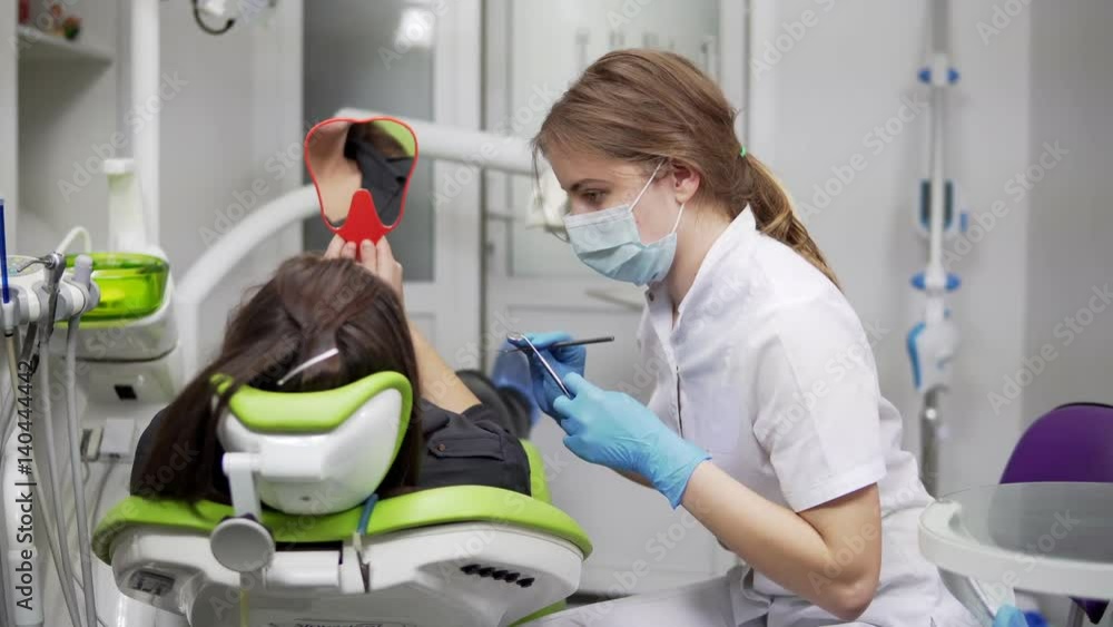 Stomatology. Young female dentist is talking to a client, giving her a mirror. Stomatology. Young female dentist is talking to a client, giving her a mirror.