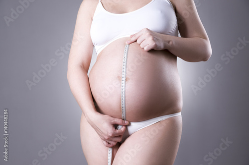 Pregnancy and nutrition - pregnant woman with measuring tape on gray background