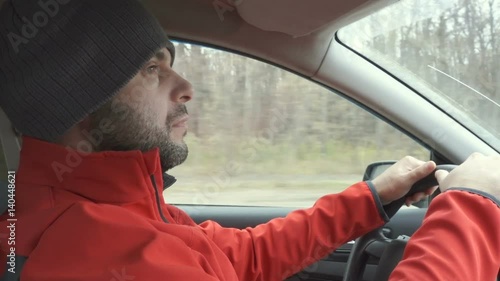 A man in a red jacket drives a car. Close up profile shot photo