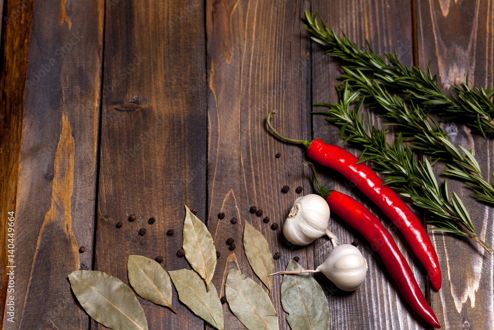 Red chili pepper and rosemary sprigs with laurel leaves and white garlic heads on wooden background