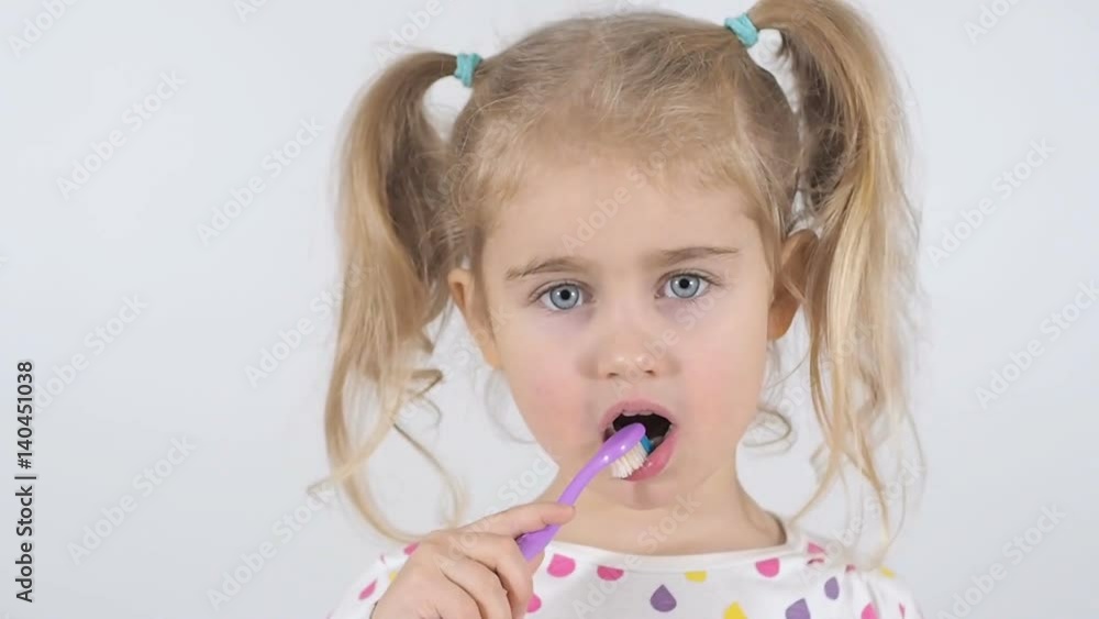 Cute little girl with pigtails diligently brushing his teeth. In the hand of the girl has toothbrush. Cheerful girl looking into the camera. Cute little girl with pigtails diligently brushing his teeth. In the hand of the girl has toothbrush. Cheerful girl looking into the camera.