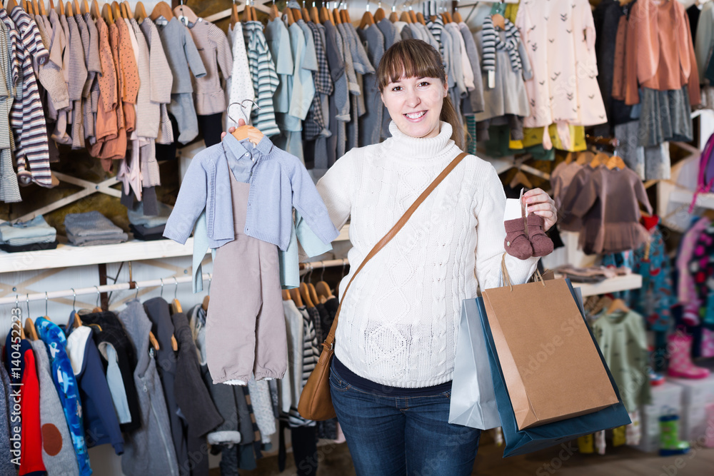 Glad pregnant mother choosing clothes for baby