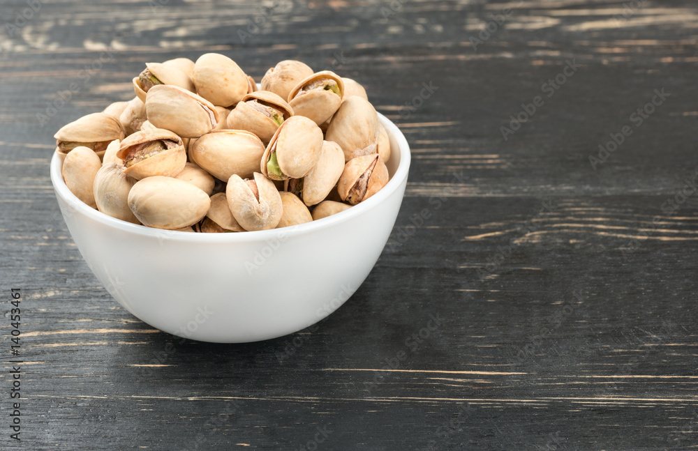 White ceramic bowl with pistachio nuts on a wooden background White ceramic bowl with pistachio nuts on a wooden background