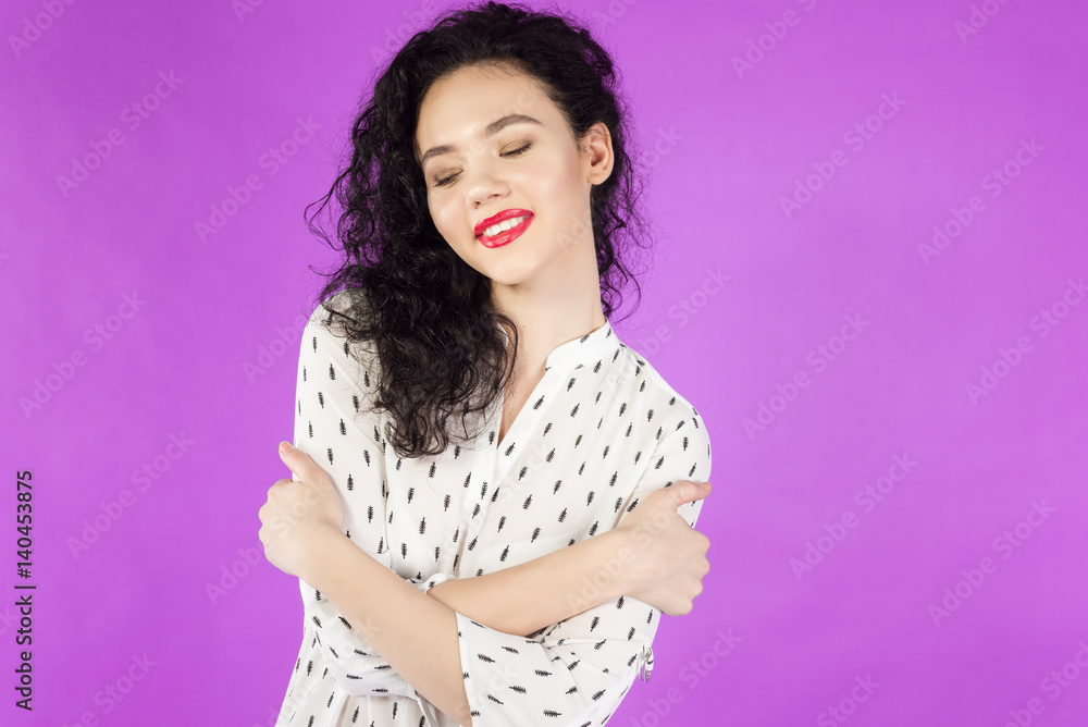 young curly brunette woman hugging herself on a pink background young curly brunette woman hugging herself on a pink background