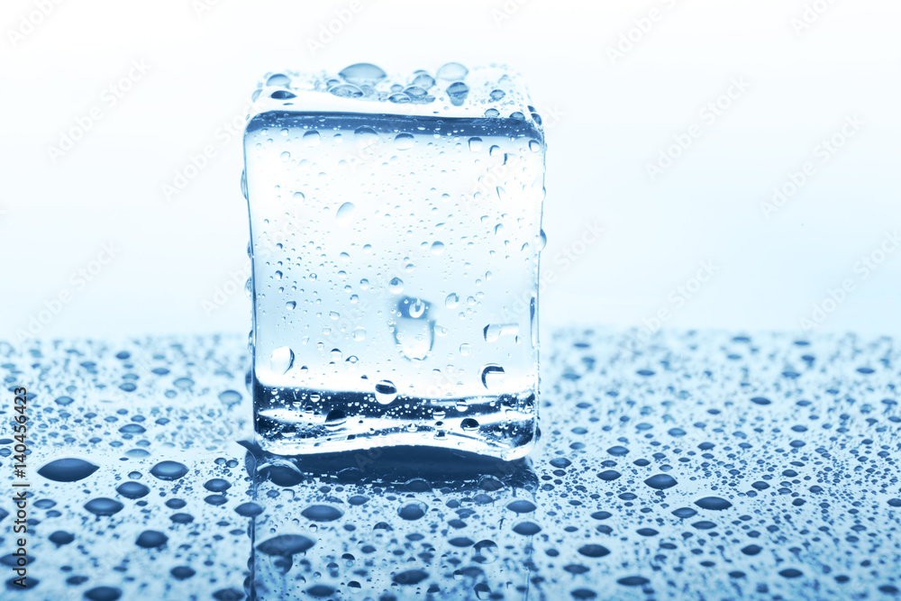 Transparent ice cube with reflection on blue glass with water drops Transparent ice cube with reflection on blue glass with water drops