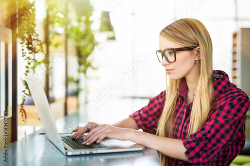 Young female entrepreneur working sitting at a desk typing on her laptop computer in a office, view from side Free Download Young female entrepreneur working sitting at a desk typing on her laptop computer in a office, view from side - GFXLoad