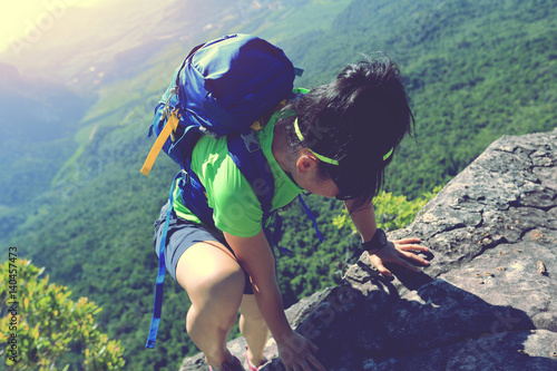 young woman hiker climbing at mountain peak rock