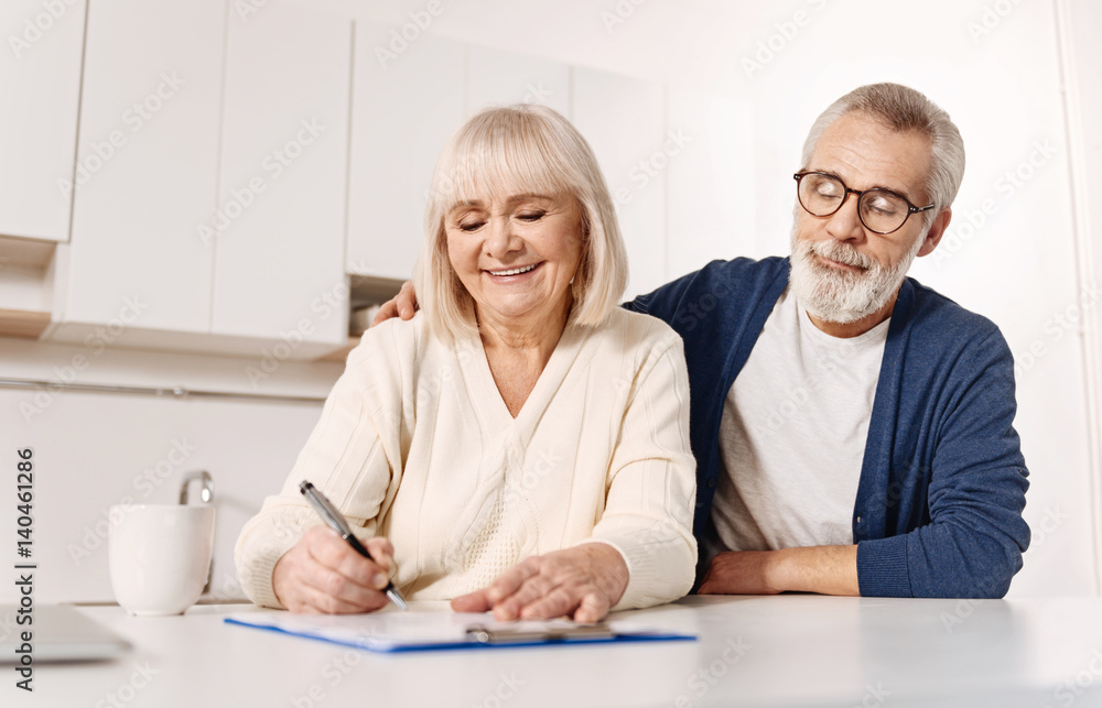 Harmonious aged couple signing documents at home Harmonious aged couple signing documents at home