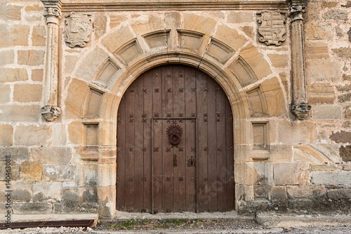 Puerta antigua de madera y fachada con escudos y columnas.