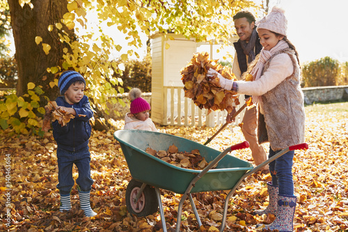 Children Helping Father To Collect Autumn Leaves In Garden
