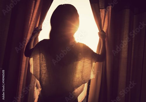 young woman stand in the room open curtain see sunrise