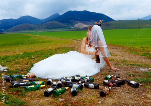 Fotografija drunken bride with lots of empty beer bottles in mountain landscape - funny wedding concept