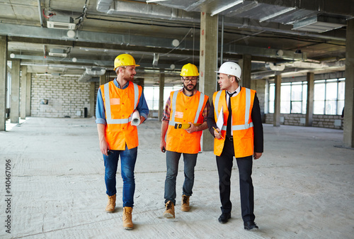 Group of contractors walking down concrete floor of unfinished construction and having talk