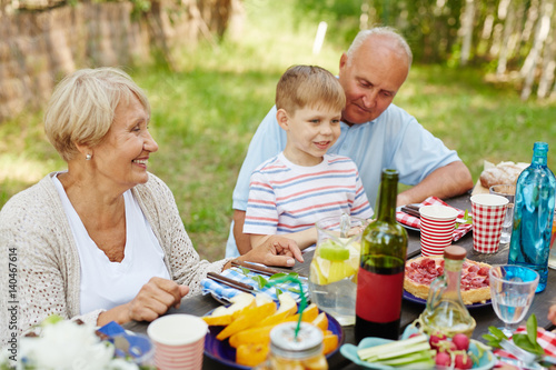 Little boy and his grandparents sitting by Thanksgiving table outdoors