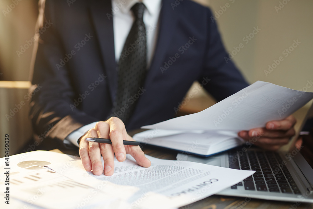 Obraz premium Closeup portrait of unrecognizable successful businessman wearing black formal suit reviewing finance statistics and contract documents at desk