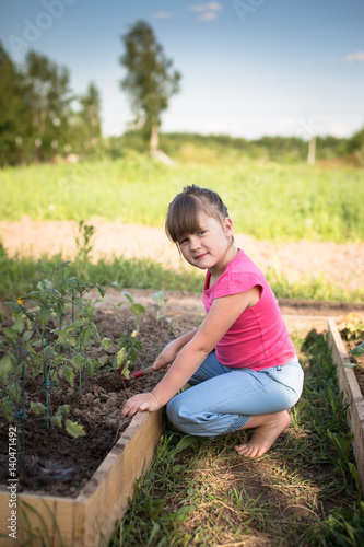 Child girl cares for vegetables on garden, ecology