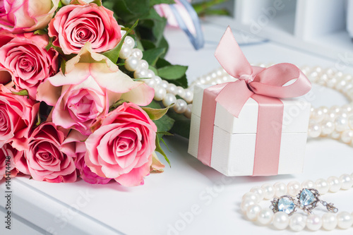 Present box with pink ribbon and jewellery with fresh roses on white table