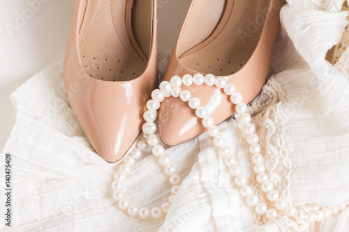 Female accessories - white dress, nude shoes close up on white leather chair still life