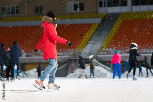 Woman in a red jacket on a skating rink in the evening