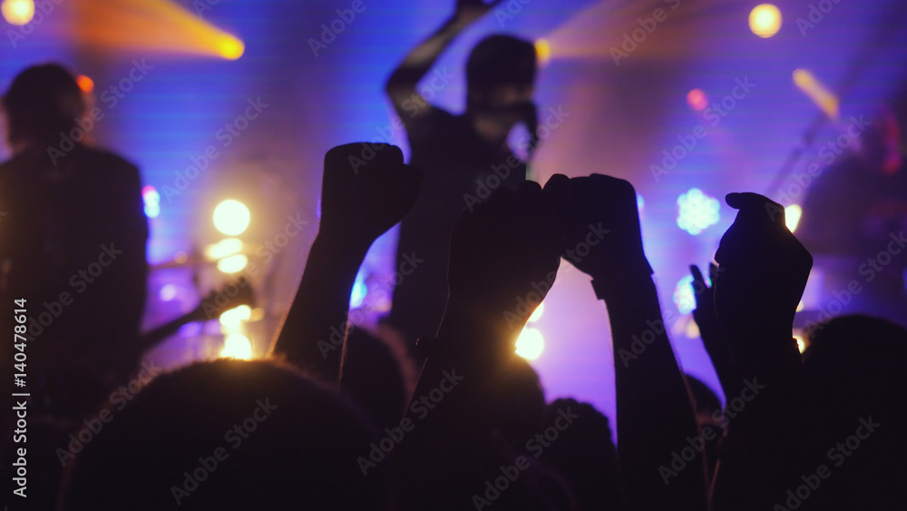 Fans waving their hands at rock concert in night club on beautiful golden lights in a purple colors