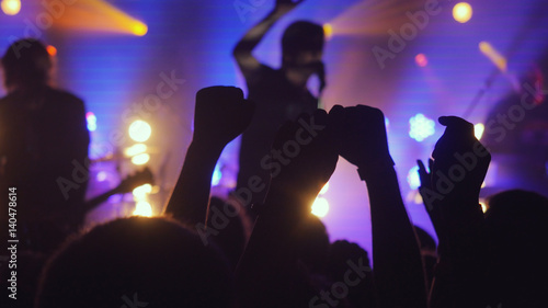 Fans waving their hands at rock concert in night club on beautiful golden lights in a purple colors