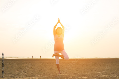 silhouette of pregnant mother performing yoga on beach during sunset