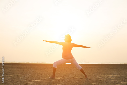 silhouette of pregnant mother performing yoga on beach during sunset
