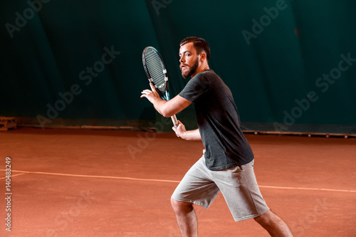 Handsome young man in t-shirt holding tennis racket on tennis court