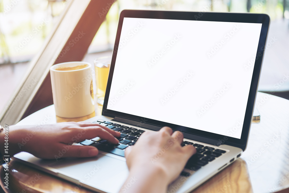 Mockup image of hands using laptop with blank white screen on vintage wooden table in cafe Mockup image of hands using laptop with blank white screen on vintage wooden table in cafe