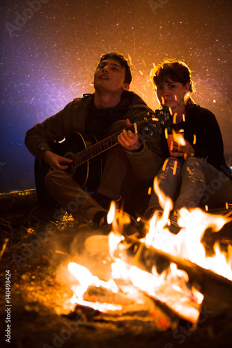 man plays guitar and woman about the fire on the background of the starry sky