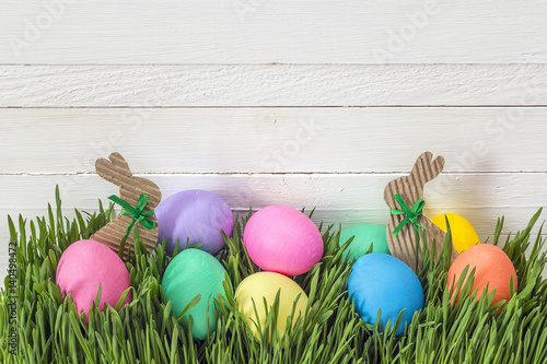 Easter eggs in fresh green grass on white  wooden background.