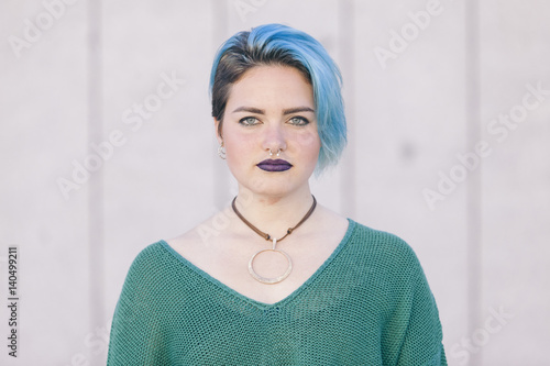 Teen androgynous woman with sad expression and blue dyed hair isolated on the street