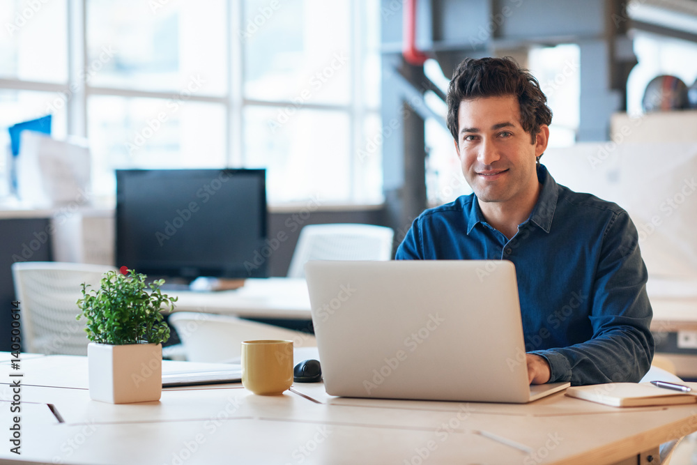 Smiling young businessman working on a laptop in an office Smiling young businessman working on a laptop in an office