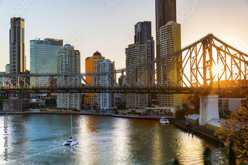 Yacht passing under Brisbane Story Bridge as the sunsets behind the cityscape © Bostock