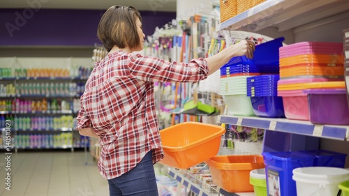 A young woman in check shirt is choosing plastic box in the shopping center. 4k