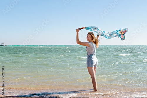 Beautiful blonde girl, woman with silk shawl on sea beach. Travel and vacation concept.