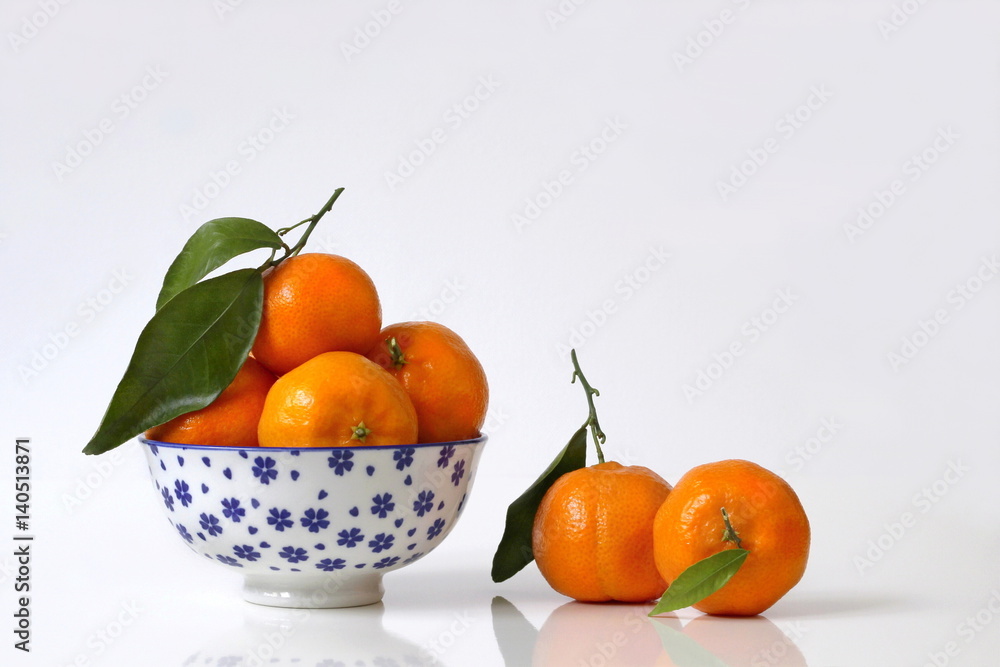 Fresh mandarin orange fruits with leaves in a chinese bowl on a white background. Home kitchen still life with orange tangerine fruits in a blue decorated bowl. Kitchen fruit decoration. Fresh mandarin orange fruits with leaves in a chinese bowl on a white background. Home kitchen still life with orange tangerine fruits in a blue decorated bowl. Kitchen fruit decoration.