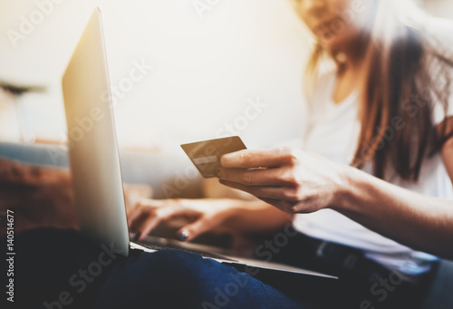 Closeup of female hands holding credit card to pay online via modern laptop, hipster girl with long hair using debit card paying for shopping online in internet, flare light photo