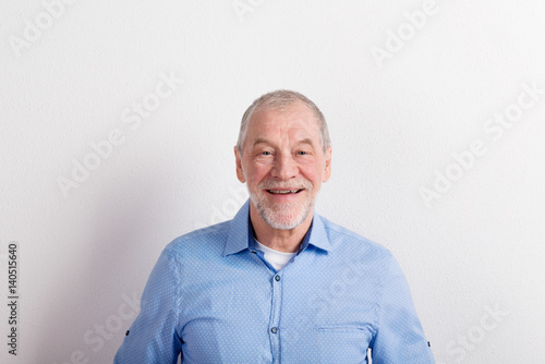 Senior man in light blue shirt smiling, studio shot. © Halfpoint