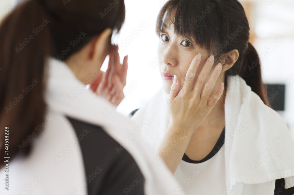 Sporty woman looking at herself in mirror, touching her face Sporty woman looking at herself in mirror, touching her face