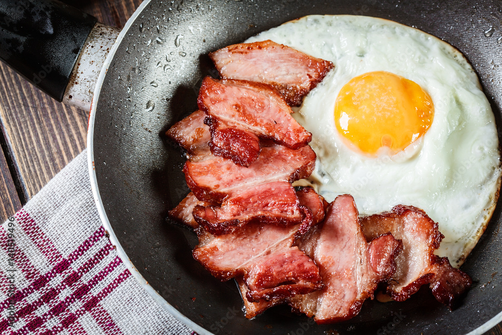 Slices of smoked bacon and fried egg in frying pan Slices of smoked bacon and fried egg in frying pan