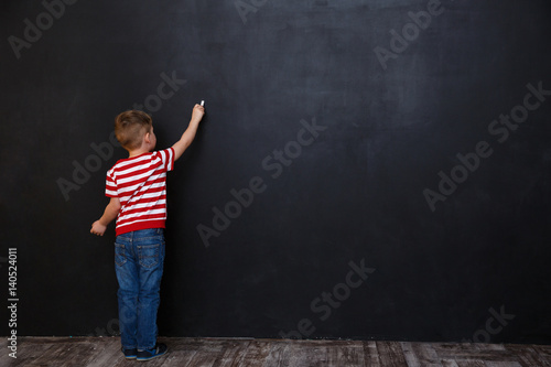 Back view of cute little kid boy writing with chalk